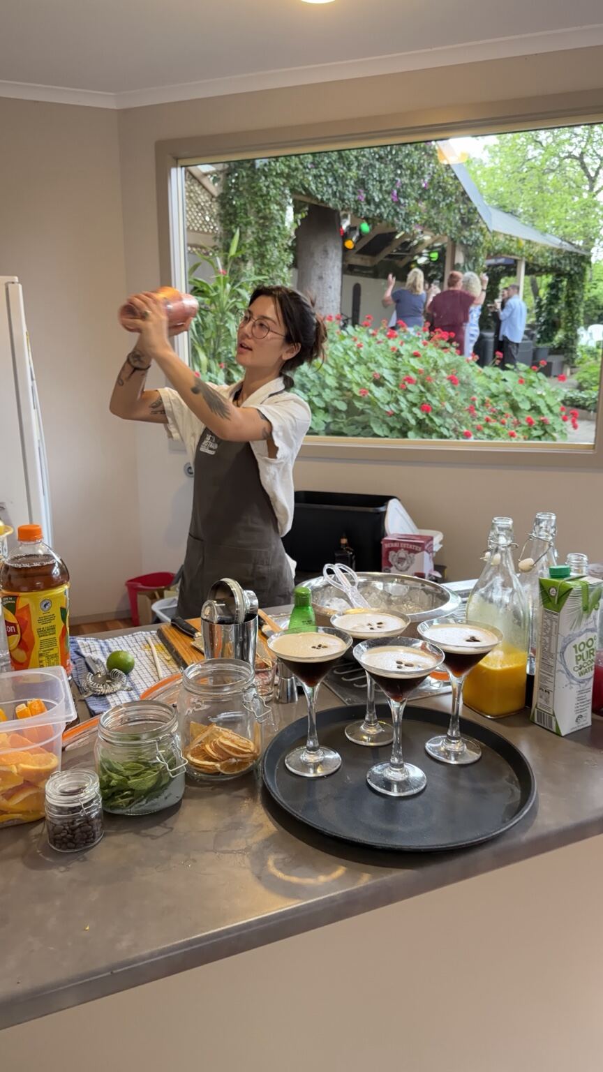 A bartender shaking a cocktail behind freshly poured espresso martinis